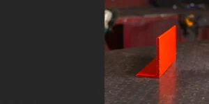 Red rolled steel angle resting on a black counter, highlighting its precise L-shaped profile. The vibrant red coating emphasizes its durability and suitability for structural and support applications. This rolled steel angle is a versatile and reliable choice for construction and engineering projects.