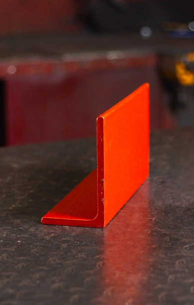 Red rolled steel angle resting on a black counter, highlighting its precise L-shaped profile. The vibrant red coating emphasizes its durability and suitability for structural and support applications. This rolled steel angle is a versatile and reliable choice for construction and engineering projects.