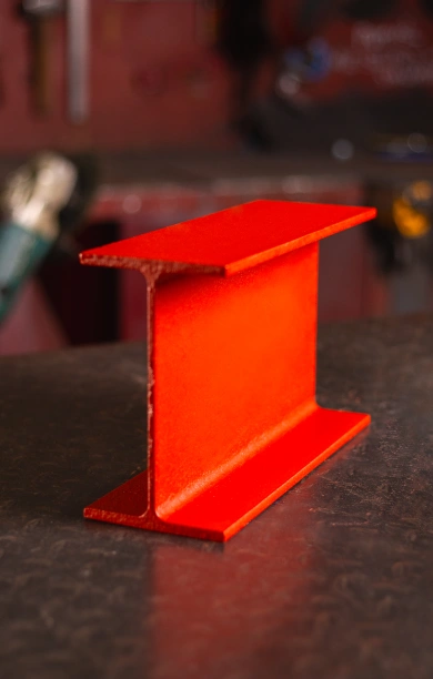 Red universal beam resting on a sleek black counter, showcasing its strong and versatile design. The bold red finish highlights its durability and suitability for structural applications. This universal beam is ideal for projects requiring strength and reliability in construction.